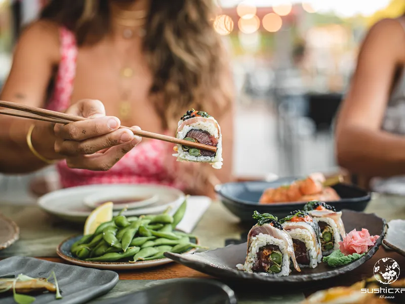 Foto de portada de SushiCafé con una mujer disfrutando de sushi, que capta la experiencia gastronómica y sus deliciosas propuestas.