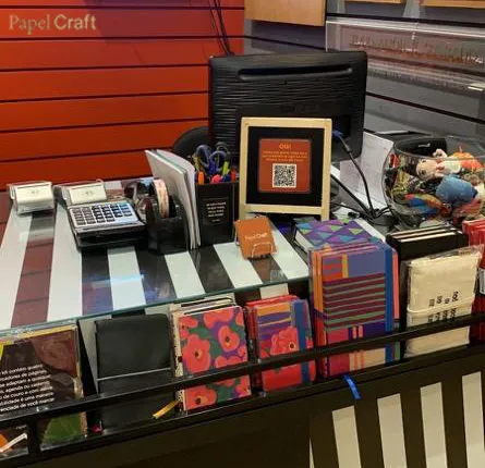 Soporte enmarcado con código QR para reseñas en el mostrador de caja de Papel Craft, junto al terminal de tarjetas y los expositores de libretas