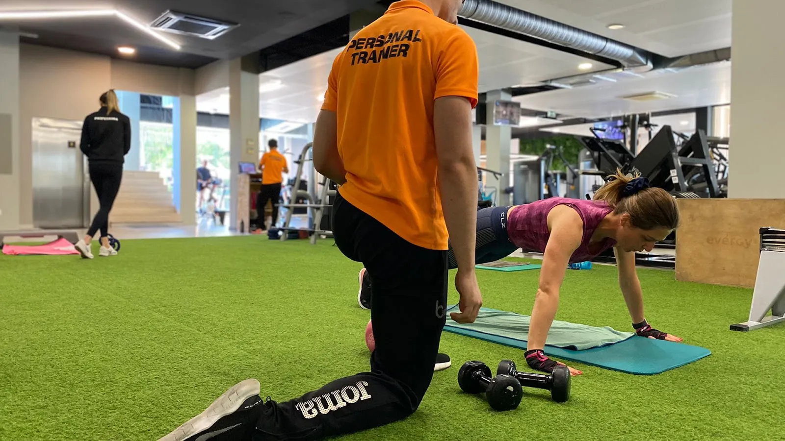 Un entrenador personal guiando a un cliente en un ejercicio de suelo sobre el césped del gimnasio en un club de Balance Company