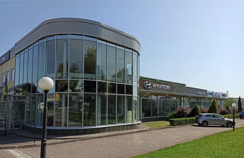 Exterior del concesionario Bogdan Auto: una sala de exhibición de cristal curvo junto a un edificio de servicio de la marca Hyundai