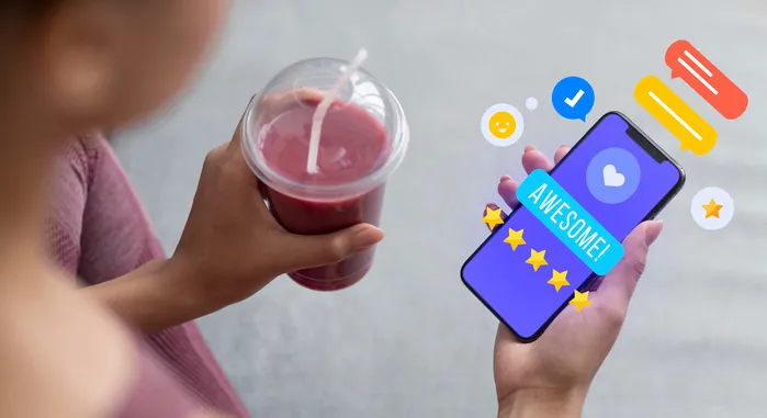 Una clienta con un batido en la mano escribe en su teléfono una reseña de cinco estrellas: "¡Genial!"
