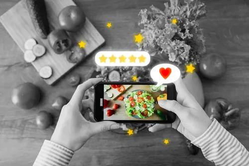 Comensal fotografiando una ensalada emplatada con el teléfono, con cinco estrellas y un corazón superpuestos